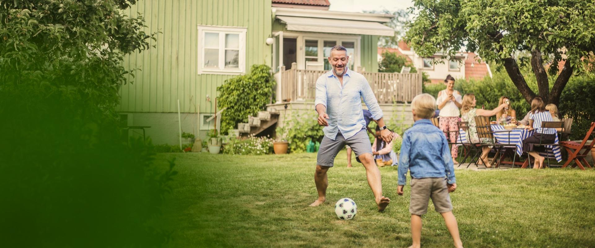 En pappa spelar fotboll med sin son i trädgården